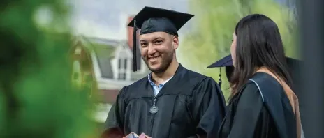 Graduate on stage smiling in cap and gown.